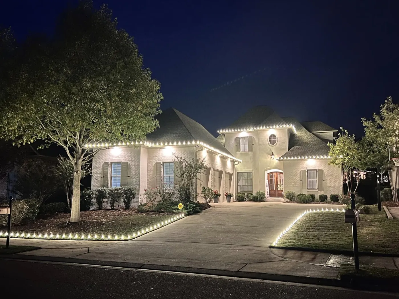 Large home at night with white lights outlining the roofline and driveway edge