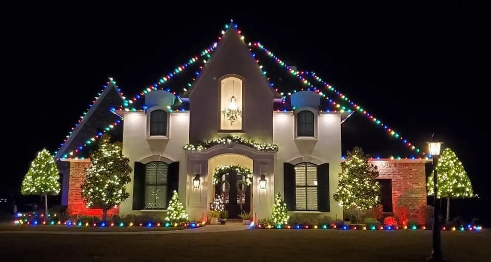 Home at night with multicolor lights outlining the gables and lit trees in the yard