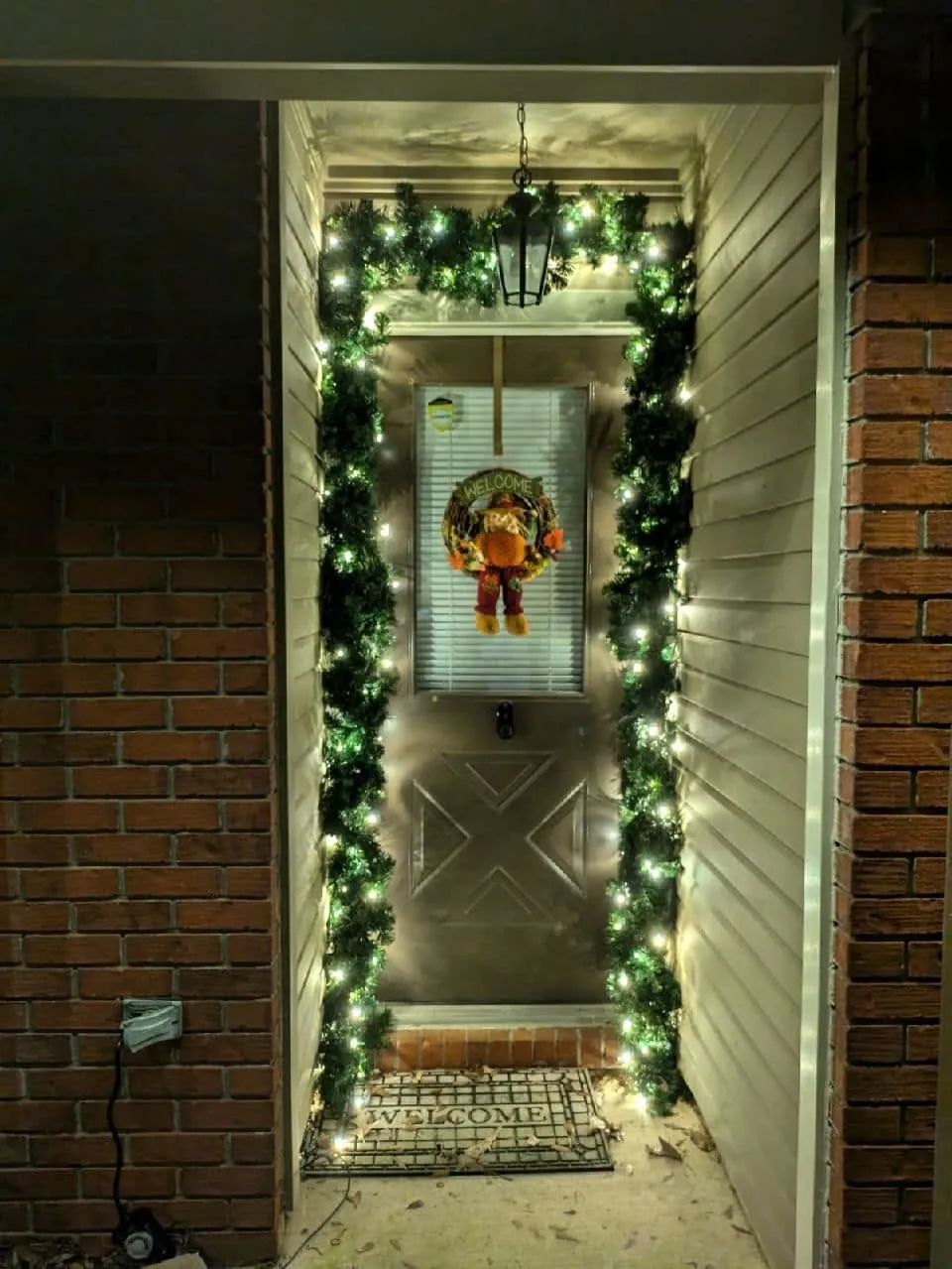 Front doorway framed by lit garland with a wreath on the door